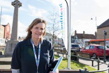 Female volunteer wearing a Healthwatch t shirt and lanyard standing in front of a flag