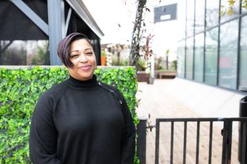 Woman wearing black stood in front of a hedge and building smiling at the camera